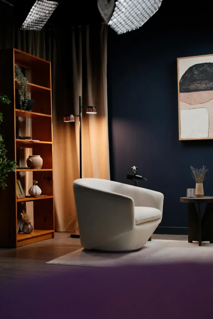 white modern chair in a cozy room recording studio with book shelves, a lamp and dark walls.